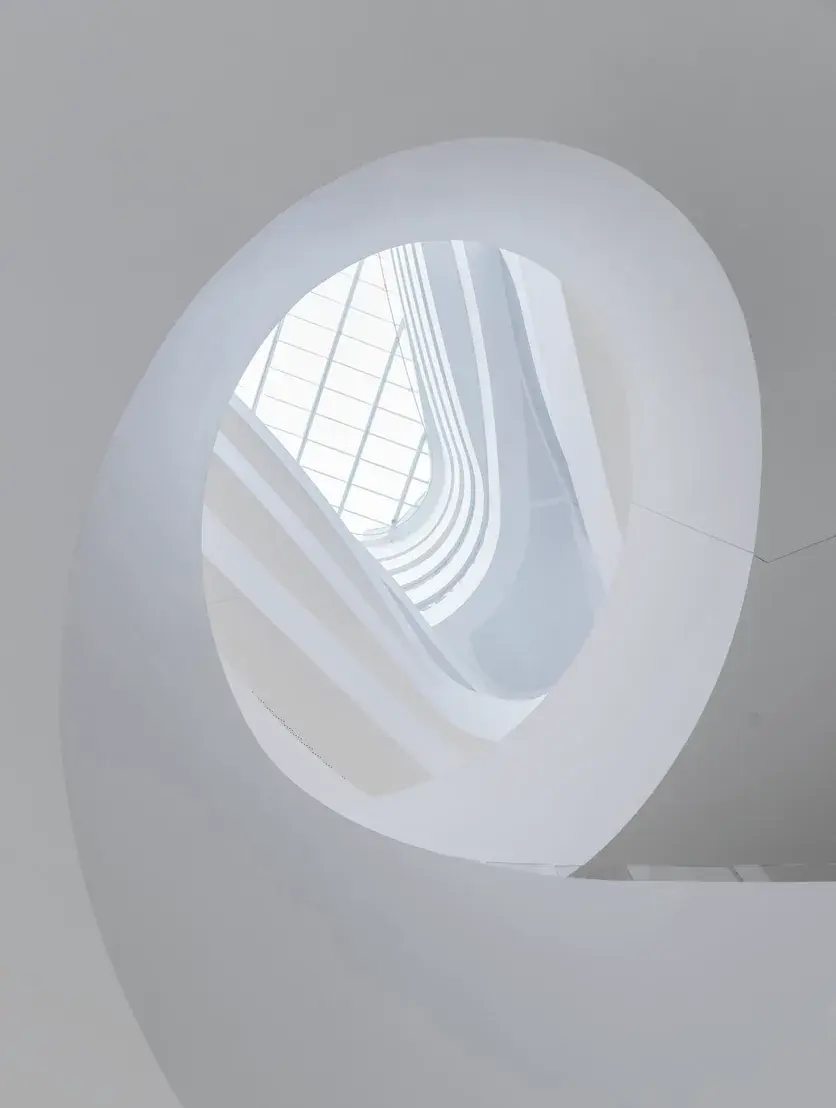 Looking up a white spiral stair to a skylight, every level visible from below