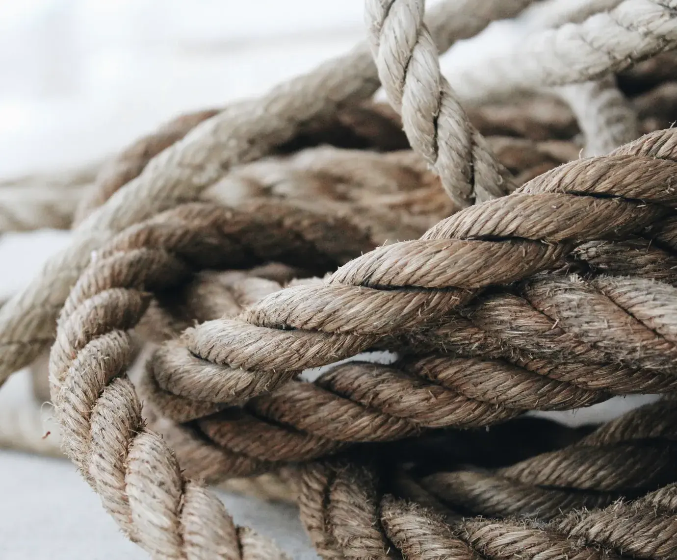 Close-up of loose, tangled lengths of natural fibre rope on a pale surface