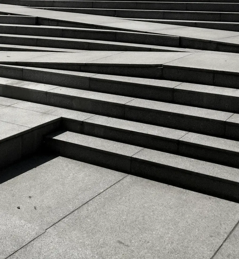 Grey stone steps and ramps rising in successive flights under hard sunlight