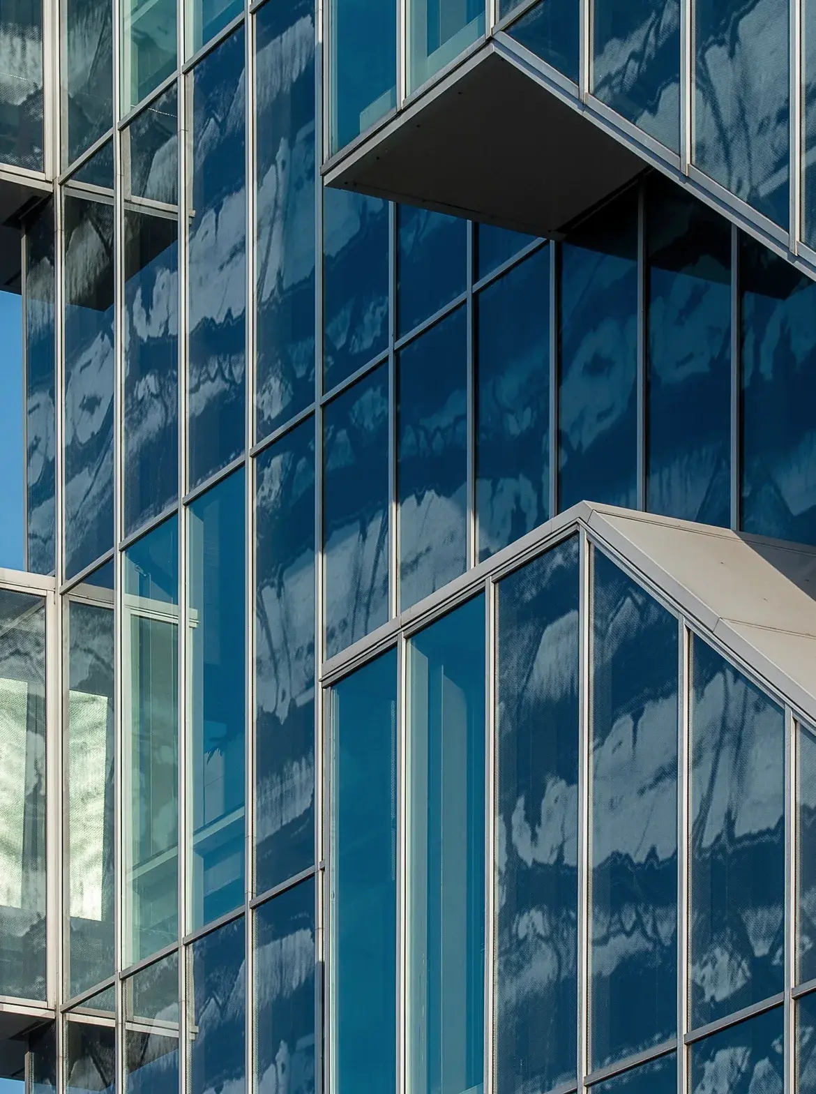 Blue glass curtain wall with cantilevered glass boxes stacked against a clear sky